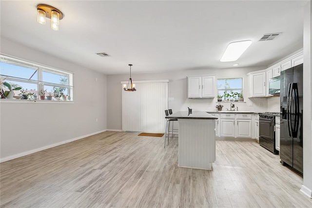 kitchen with a wealth of natural light, white cabinets, a center island, light hardwood / wood-style floors, and black appliances