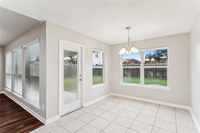 unfurnished dining area featuring plenty of natural light, light tile patterned floors, a textured ceiling, and a chandelier