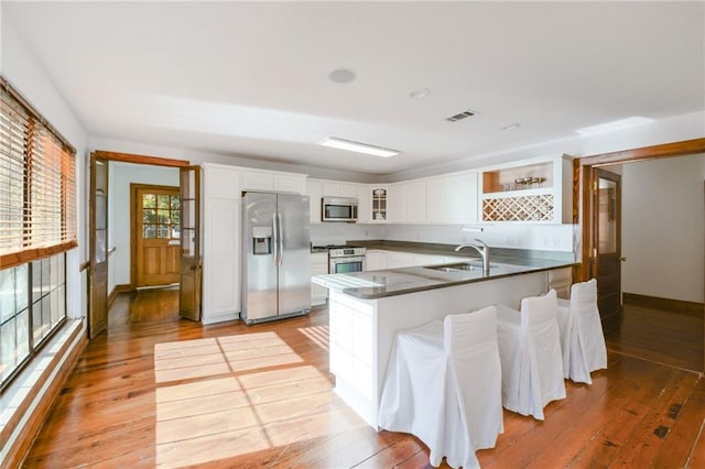 kitchen with sink, white cabinetry, stainless steel appliances, kitchen peninsula, and light wood-type flooring