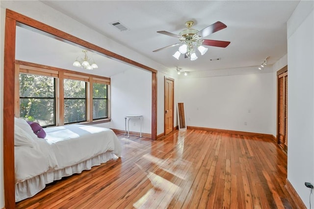 bedroom with ceiling fan with notable chandelier and light wood-type flooring