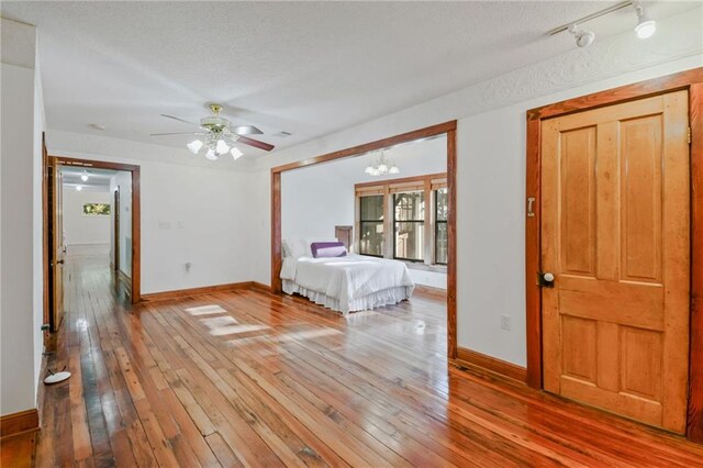 unfurnished bedroom featuring a textured ceiling, ceiling fan with notable chandelier, and hardwood / wood-style flooring