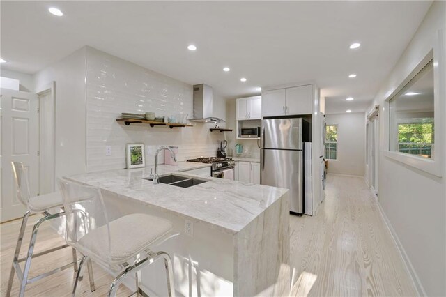 kitchen with kitchen peninsula, appliances with stainless steel finishes, white cabinets, and wall chimney range hood