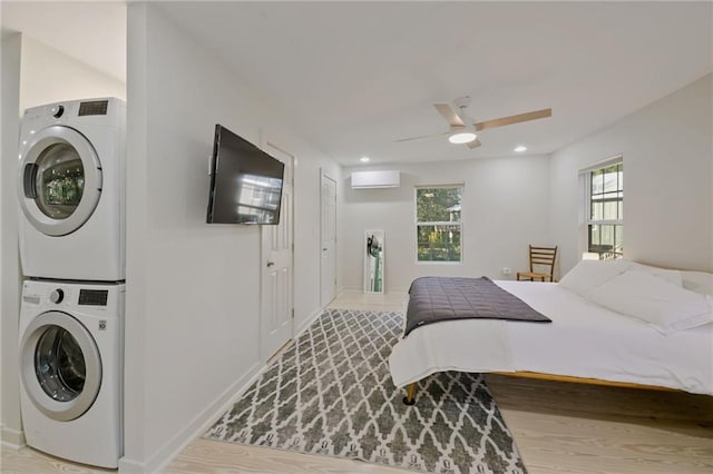 bedroom with light hardwood / wood-style floors, an AC wall unit, stacked washer / dryer, and ceiling fan