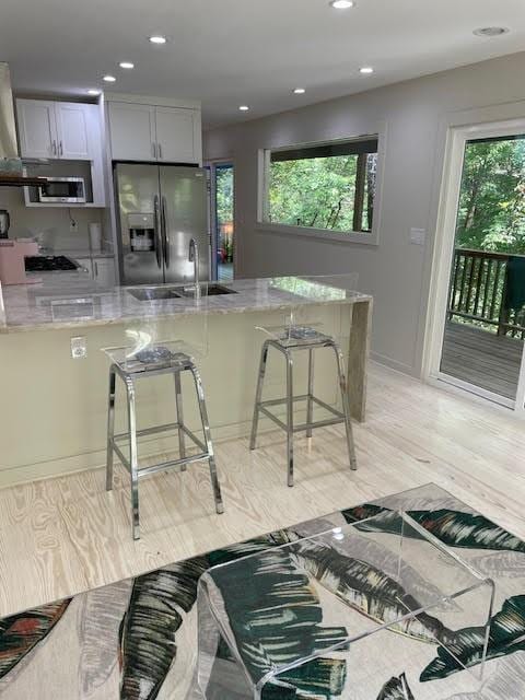 kitchen with gray cabinetry, light stone countertops, a breakfast bar area, and stainless steel appliances