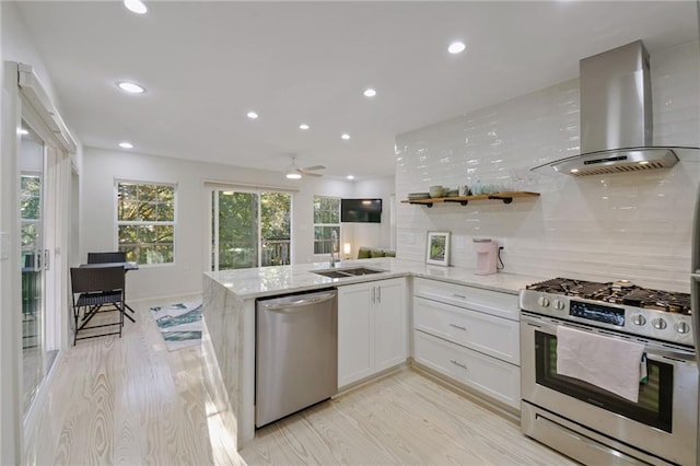 kitchen with white cabinets, stainless steel appliances, kitchen peninsula, and wall chimney exhaust hood