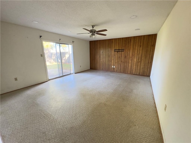 unfurnished room featuring ceiling fan, a textured ceiling, and wooden walls