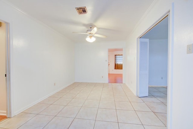 empty room featuring crown molding, light tile patterned floors, visible vents, ceiling fan, and baseboards