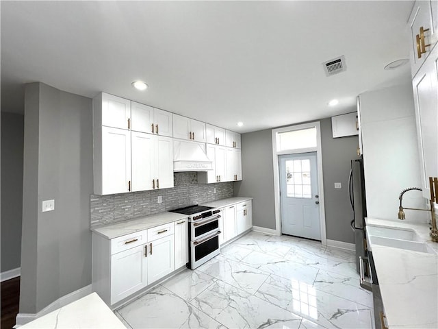 kitchen featuring white cabinetry, sink, light stone counters, custom range hood, and appliances with stainless steel finishes