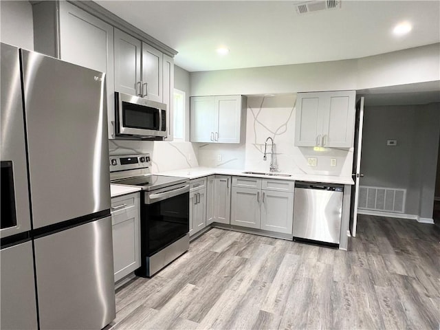 kitchen with gray cabinets, sink, stainless steel appliances, and light hardwood / wood-style flooring