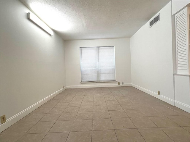 tiled empty room with a textured ceiling and baseboards