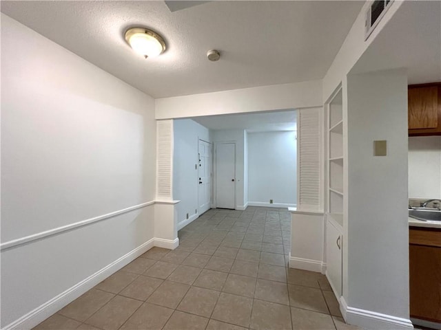 hall with light tile patterned floors, baseboards, a sink, and a textured ceiling