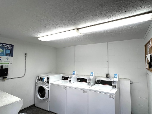 shared laundry with separate washer and dryer, concrete block wall, and a textured ceiling