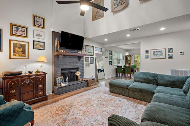 living room featuring a fireplace, ceiling fan, light hardwood / wood-style flooring, and a towering ceiling