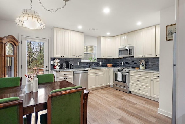 kitchen featuring light wood-type flooring, decorative light fixtures, light stone counters, white cabinetry, and stainless steel appliances