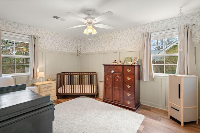 bedroom featuring ceiling fan, light wood-type flooring, a nursery area, and multiple windows