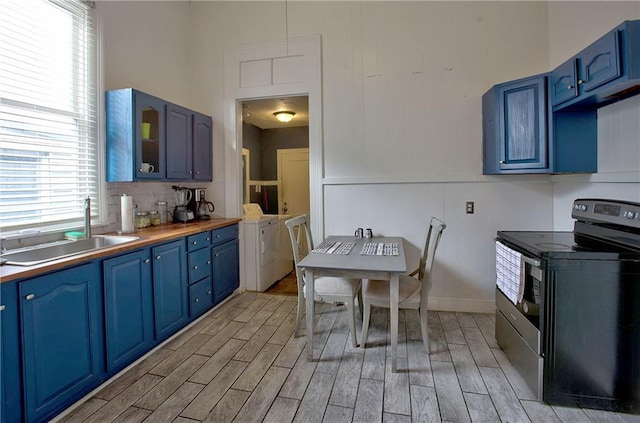 312931 N Claiborne Ave, New Orleans, LA 70117 - kitchen featuring blue cabinets, wood finish floors, a sink, stainless steel electric stove, and washing machine and clothes dryer