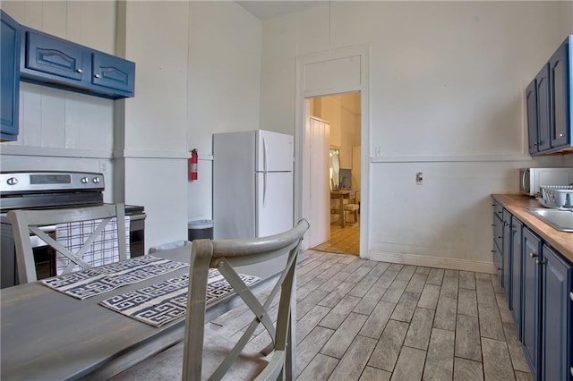 kitchen featuring blue cabinetry, butcher block counters, white refrigerator, stainless steel electric range oven, and light wood-type flooring