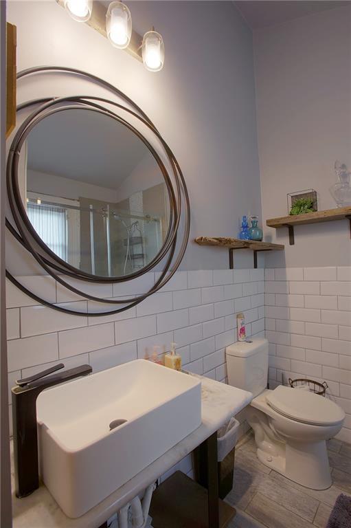 312931 N Claiborne Ave, New Orleans, LA 70117 - bathroom featuring a wainscoted wall, toilet, a sink, a shower with door, and tile walls