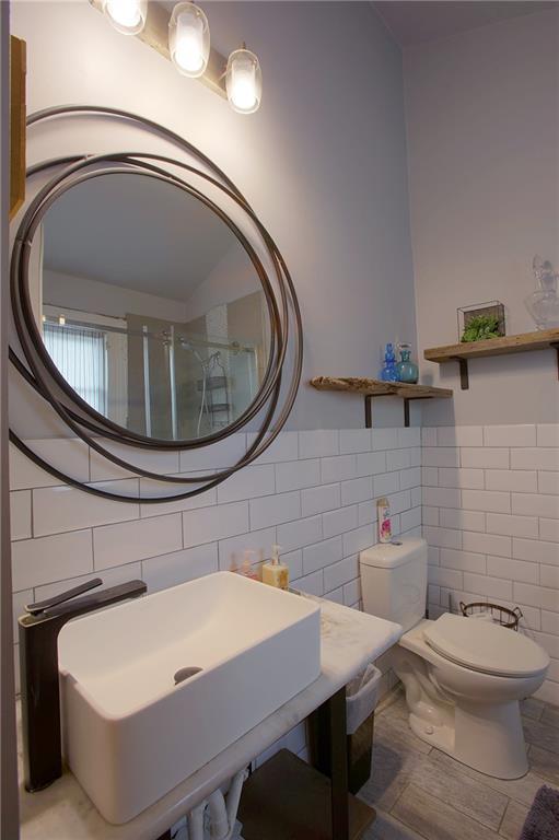 bathroom with walk in shower, sink, tile walls, and toilet