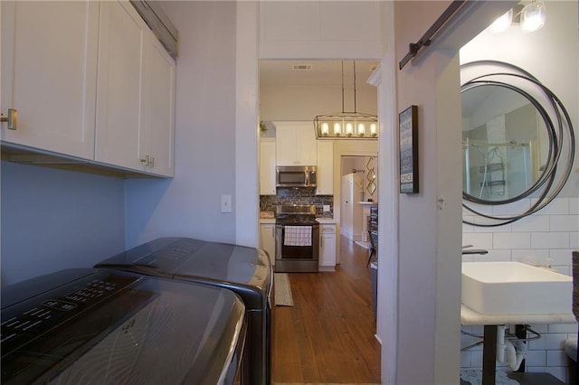 laundry area featuring sink, washing machine and dryer, cabinets, dark hardwood / wood-style floors, and a barn door