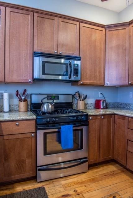 kitchen featuring light stone countertops, ceiling fan, stainless steel appliances, and light wood-type flooring