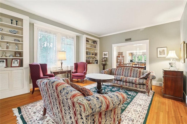 living room featuring a notable chandelier, light hardwood / wood-style floors, built in features, and crown molding