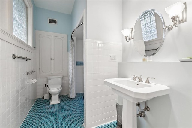 bathroom with tile patterned flooring, toilet, plenty of natural light, and tile walls