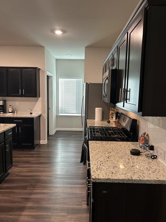 kitchen with black gas range, light stone countertops, and dark wood-type flooring