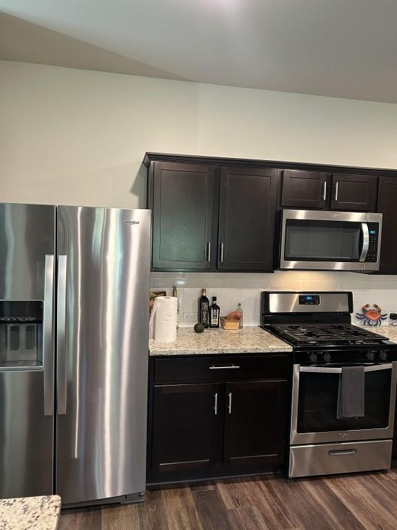 kitchen with decorative backsplash, light stone countertops, stainless steel appliances, and dark wood-type flooring