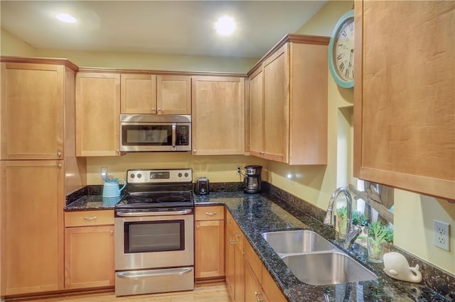 kitchen featuring light brown cabinetry, stainless steel appliances, dark stone countertops, and sink