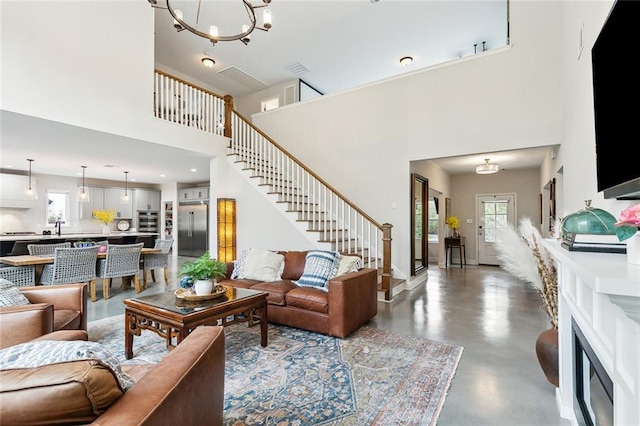 living room with concrete flooring, a towering ceiling, an inviting chandelier, and sink