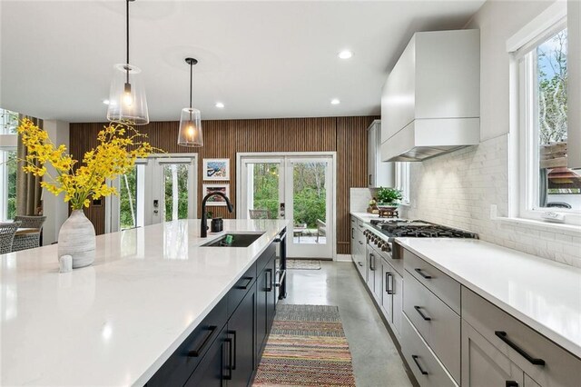 kitchen with french doors, sink, an island with sink, a healthy amount of sunlight, and custom range hood