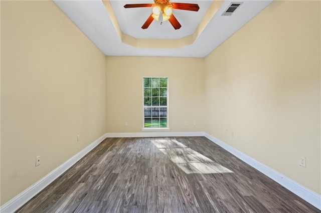 unfurnished room with a raised ceiling, ceiling fan, and dark wood-type flooring