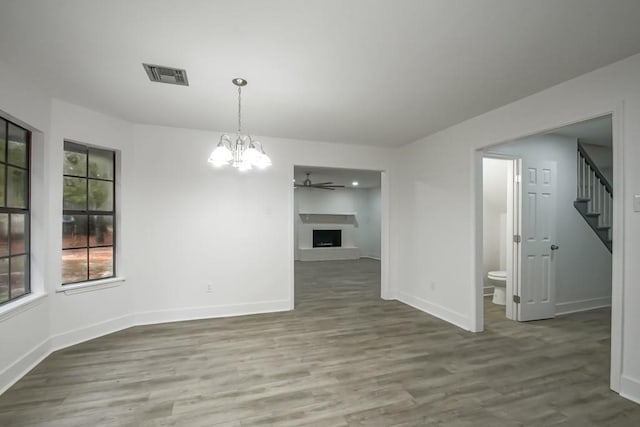 unfurnished dining area with ceiling fan with notable chandelier and wood-type flooring