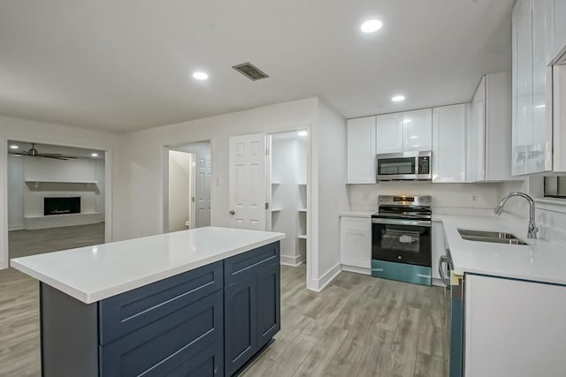 kitchen featuring sink, blue cabinets, light hardwood / wood-style floors, white cabinets, and appliances with stainless steel finishes