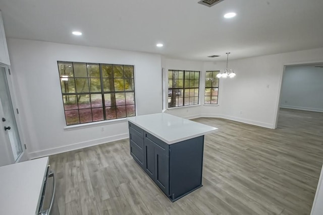 kitchen featuring light hardwood / wood-style flooring, a kitchen island, hanging light fixtures, and an inviting chandelier