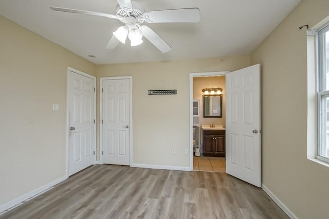 unfurnished bedroom with ceiling fan, multiple windows, connected bathroom, and light hardwood / wood-style flooring