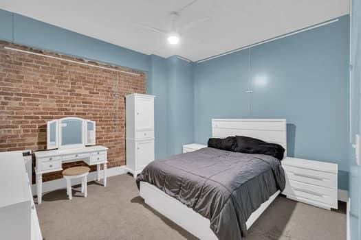 bedroom featuring ceiling fan, carpet floors, and brick wall