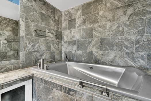 bathroom with a relaxing tiled tub and tile walls