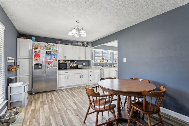 kitchen featuring stainless steel refrigerator with ice dispenser, a textured ceiling, sink, white cabinets, and hanging light fixtures