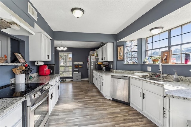 kitchen with pendant lighting, white cabinets, sink, stainless steel appliances, and a chandelier