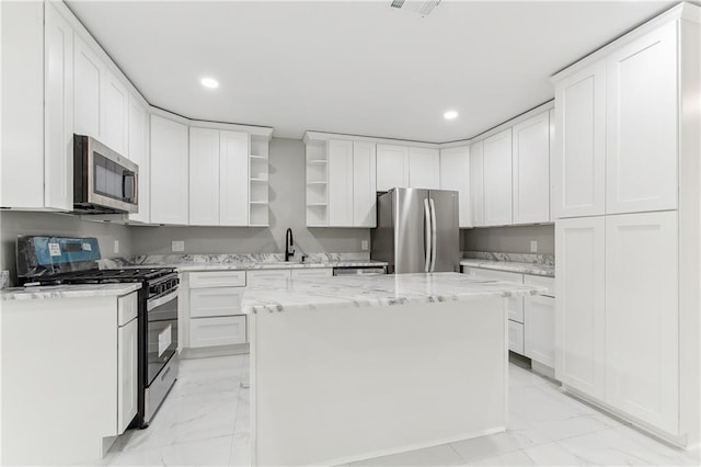 kitchen featuring a center island, sink, light stone counters, white cabinetry, and stainless steel appliances