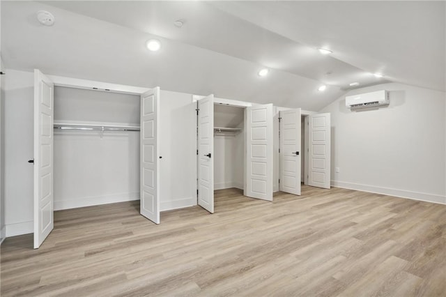 unfurnished bedroom with two closets, light wood-type flooring, lofted ceiling, and a wall mounted air conditioner