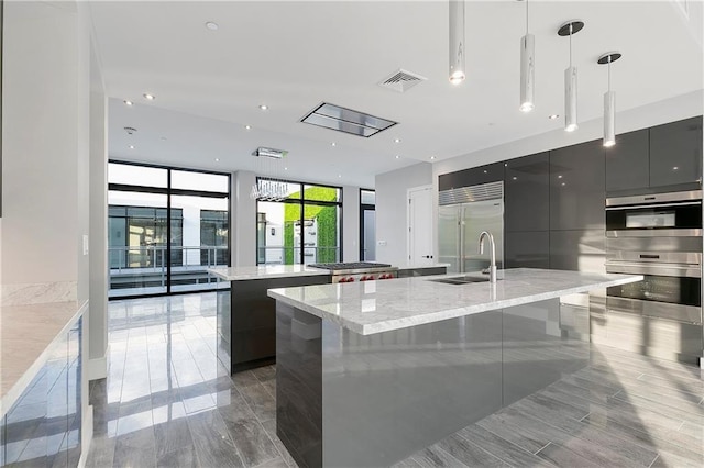 kitchen with expansive windows, stainless steel appliances, sink, hanging light fixtures, and a large island