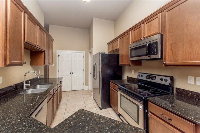 kitchen featuring light tile patterned floors, stainless steel appliances, dark stone counters, and sink