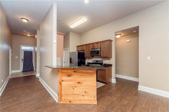 kitchen with kitchen peninsula, hardwood / wood-style floors, stainless steel appliances, and dark stone countertops