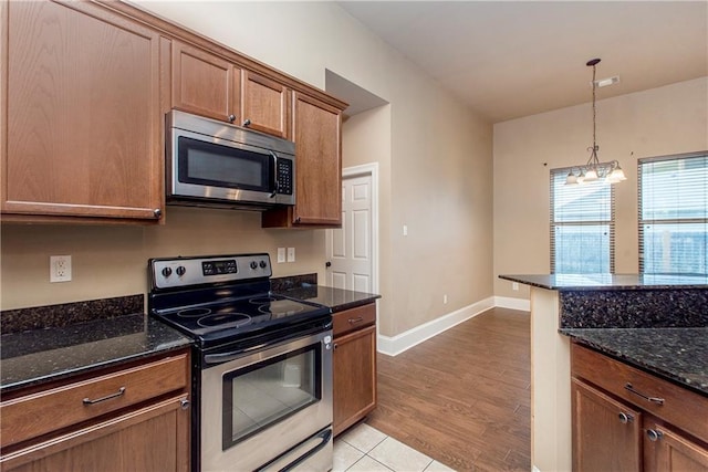 kitchen with dark stone counters, decorative light fixtures, light wood-type flooring, appliances with stainless steel finishes, and a notable chandelier