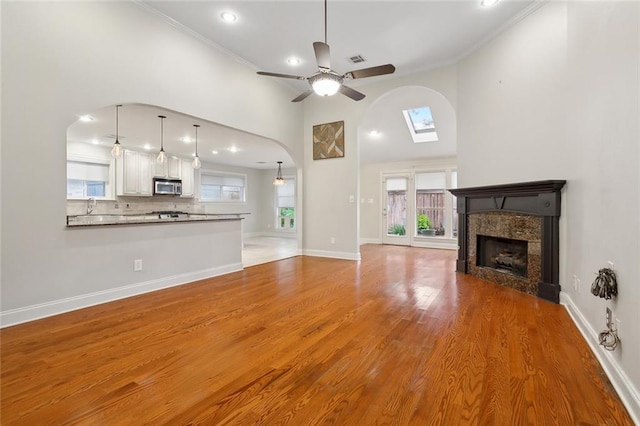 unfurnished living room featuring ceiling fan, a skylight, crown molding, and light hardwood / wood-style flooring