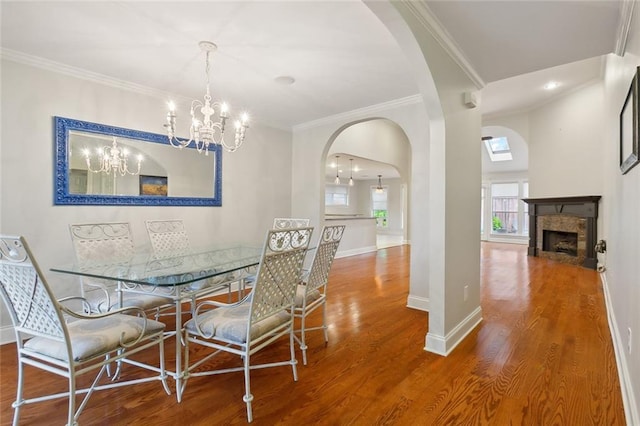 dining area featuring wood-type flooring, crown molding, a notable chandelier, and a tiled fireplace