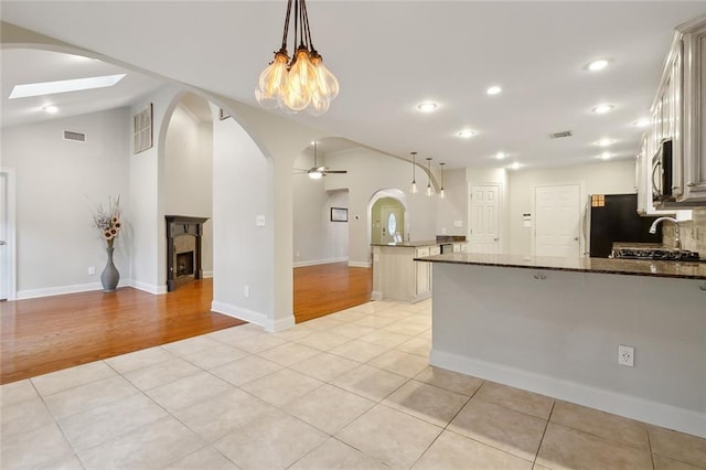 kitchen featuring ceiling fan with notable chandelier, light wood-type flooring, hanging light fixtures, and dark stone counters